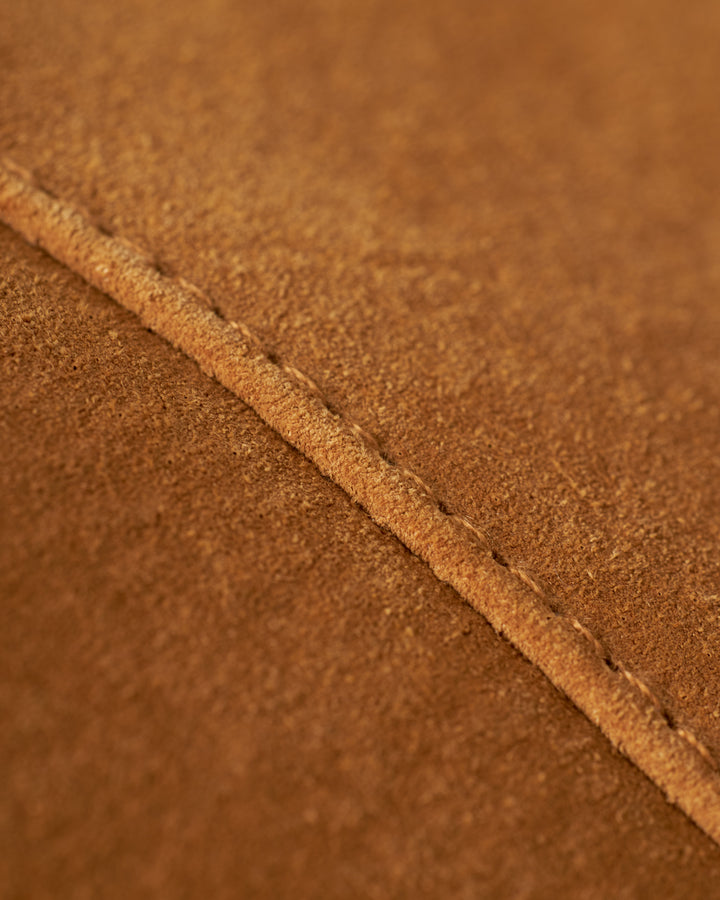 Close-up of "The Sicily Leather Skirt - Sable" by Dandy Del Mar reveals a brown leather surface with visible stitching along a seam, reminiscent of detailed craftsmanship. The texture appears slightly rough.