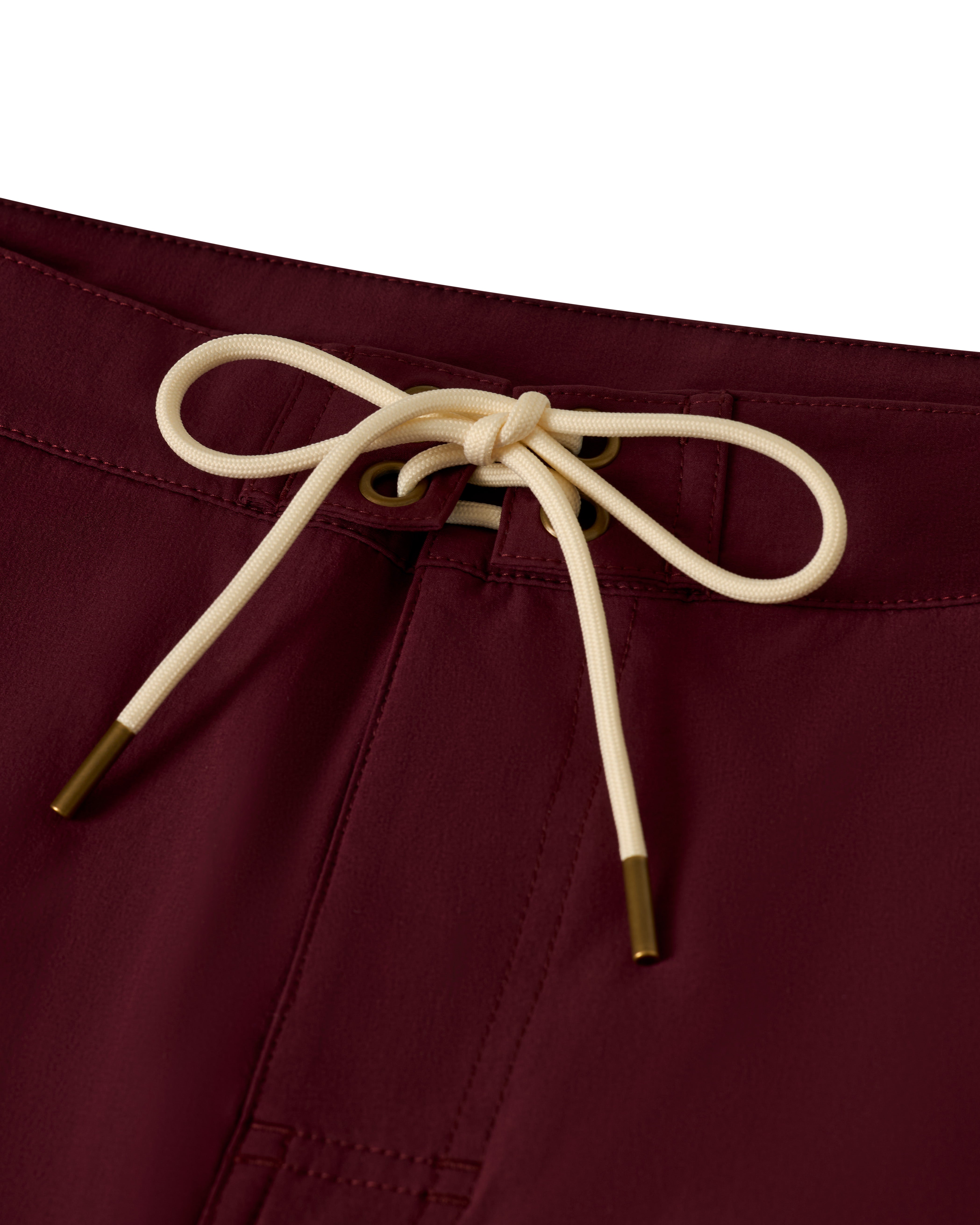 Close-up of The Stirata Swim Short by Dandy Del Mar in Bordeaux, showcasing a beige drawstring tied in a bow at the waist with brass-tipped ends.