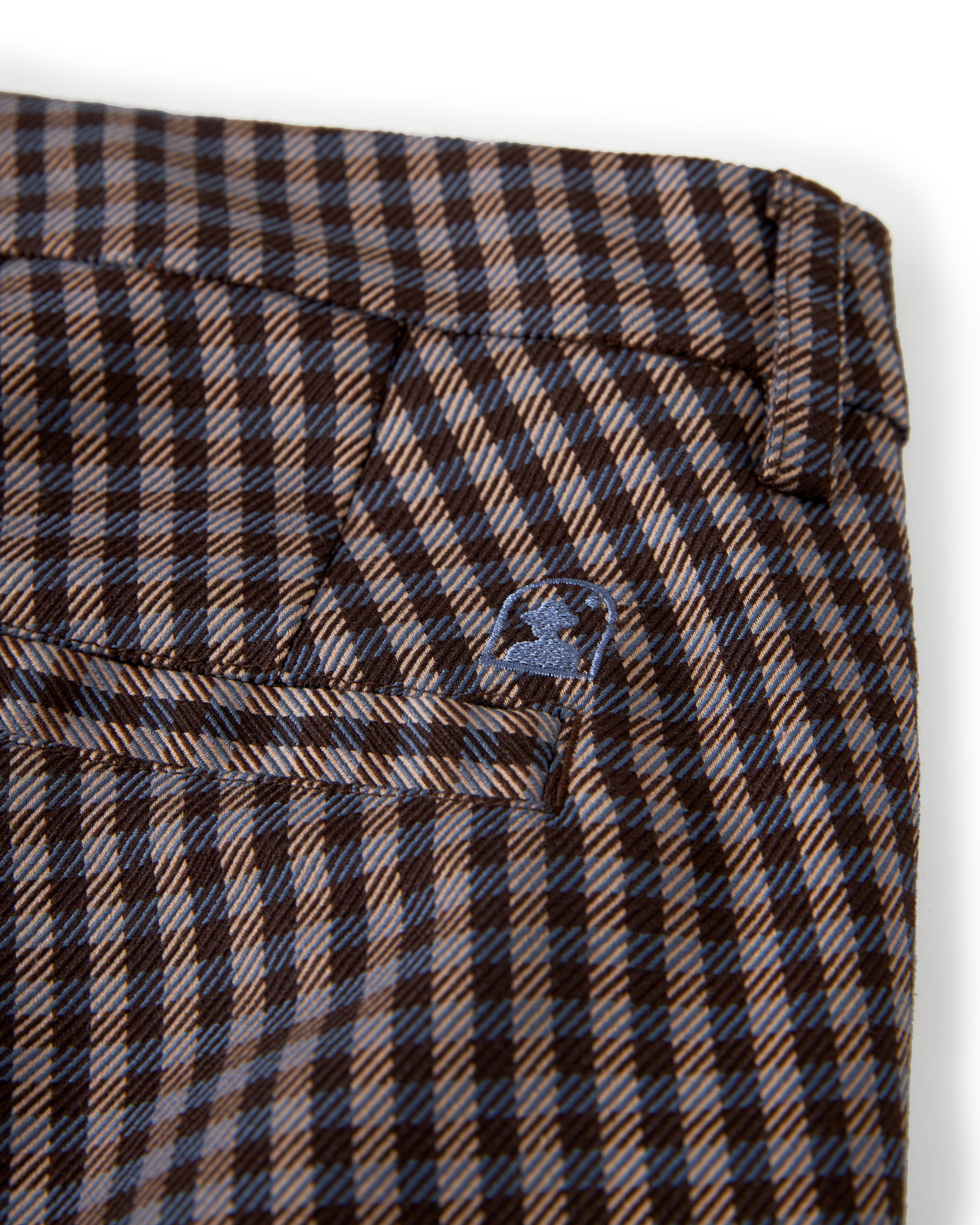 Close-up of brown and white The Tresco Trouser - Tierra Houndstooth by Dandy Del Mar, featuring a small embroidered logo on the pocket.