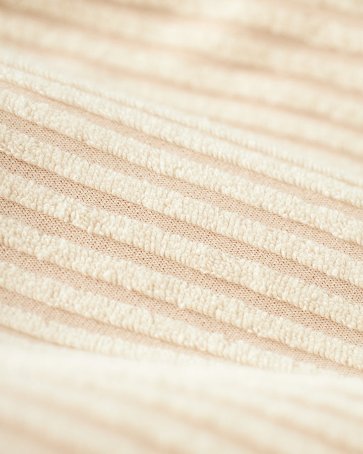 Close-up of The Tropez Jacquard Robe - Scallop Stripe by Dandy Del Mar, featuring a cream-colored ribbed fabric with a soft, textured surface and evenly spaced horizontal lines reminiscent of jacquard striped Terry Cloth.