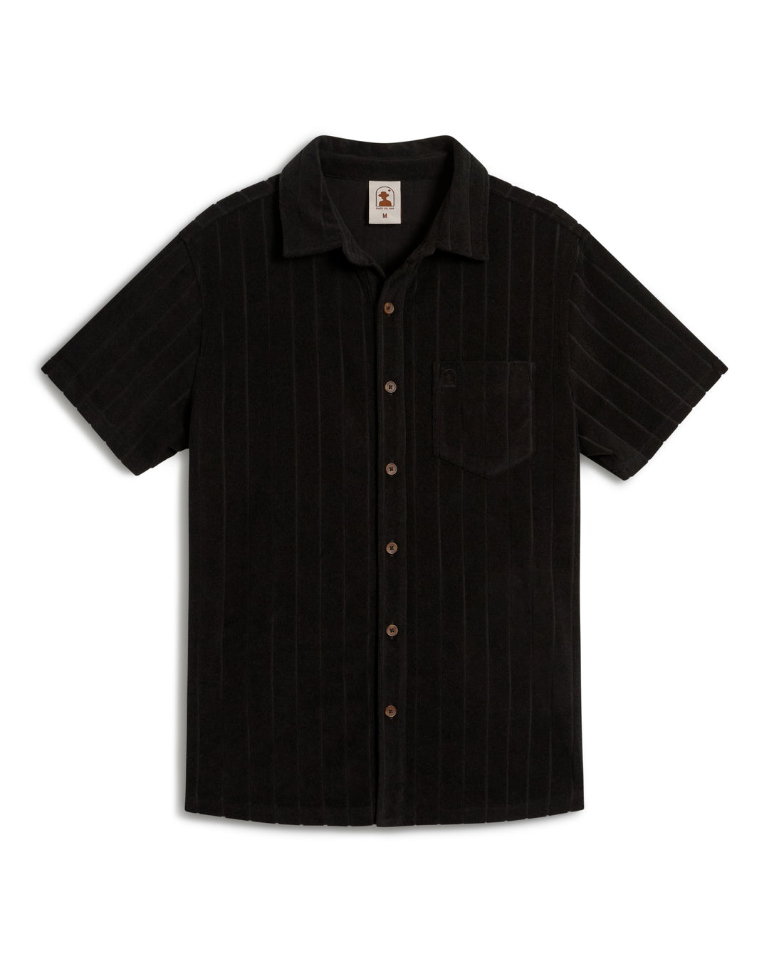 The Tropez Terry Cloth Shirt - Onyx by Dandy Del Mar is a black short-sleeve shirt featuring subtle vertical stripes, brown buttons, and a chest pocket.