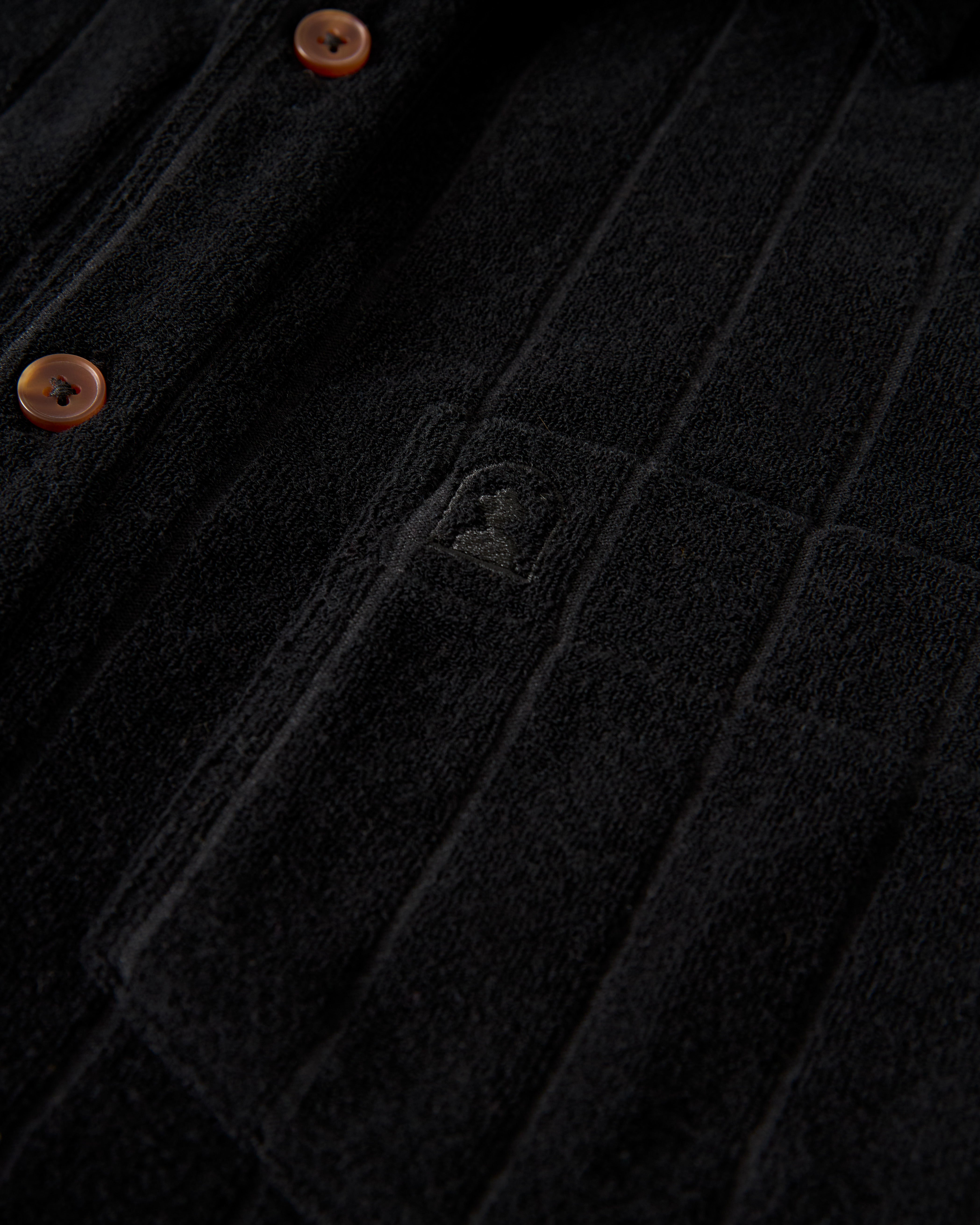 Close-up of a textured dark fabric with subtle embroidery and brown buttons, reminiscent of the luxurious Tropez Jacquard Shirt in Onyx by Dandy Del Mar.