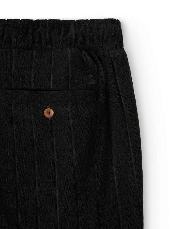 Close-up of The Tropez Terry Cloth Short - Onyx by Dandy Del Mar, featuring black ribbed fabric with an elastic waistband and a back pocket with a button.