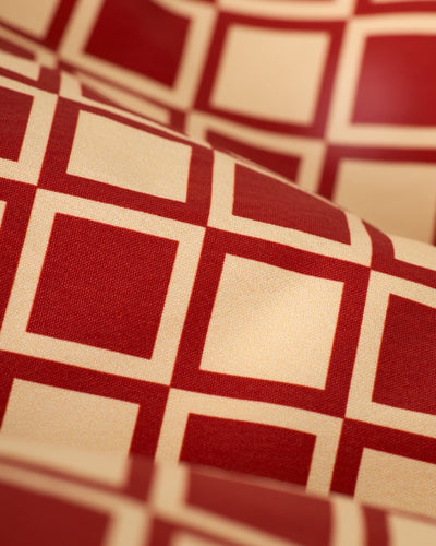 Close-up of The Ventura Volley Shorts - Rouge by Dandy Del Mar, featuring a red and beige square pattern with intersecting lines, a repeating geometric design, and an elastic waist for comfort.