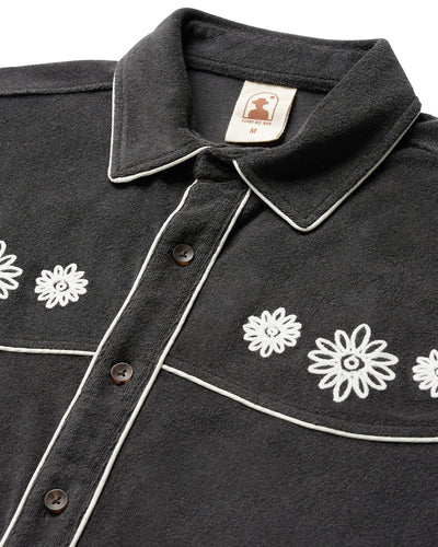 Close-up of The Gaucho Terry Cloth Shirt by Dandy Del Mar, a black button-up featuring white piping and embroidered white floral designs on the front.