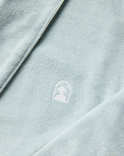 The Tropez Terry Cloth Robe by Dandy Del Mar in Gulf Blue features ultra-soft textured fabric, a small white embroidered silhouette logo in an arch, and an above-the-knee fit for comfort and style.